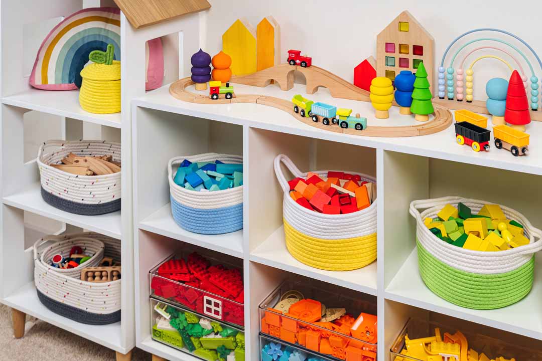 White shelving with colorful storage baskets and transparent boxes in children room. Rainbow toys in stylish baskets and plastic containers. Organizing and Storage Ideas in playroom